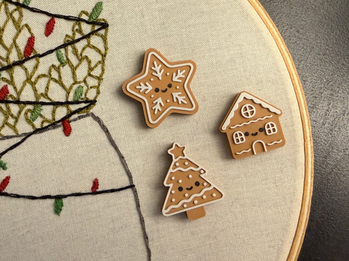 Three embroidered gingerbread cookies on a fabric hoop with Christmas tree design.