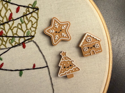 Three embroidered gingerbread cookies on a fabric hoop with Christmas tree design.